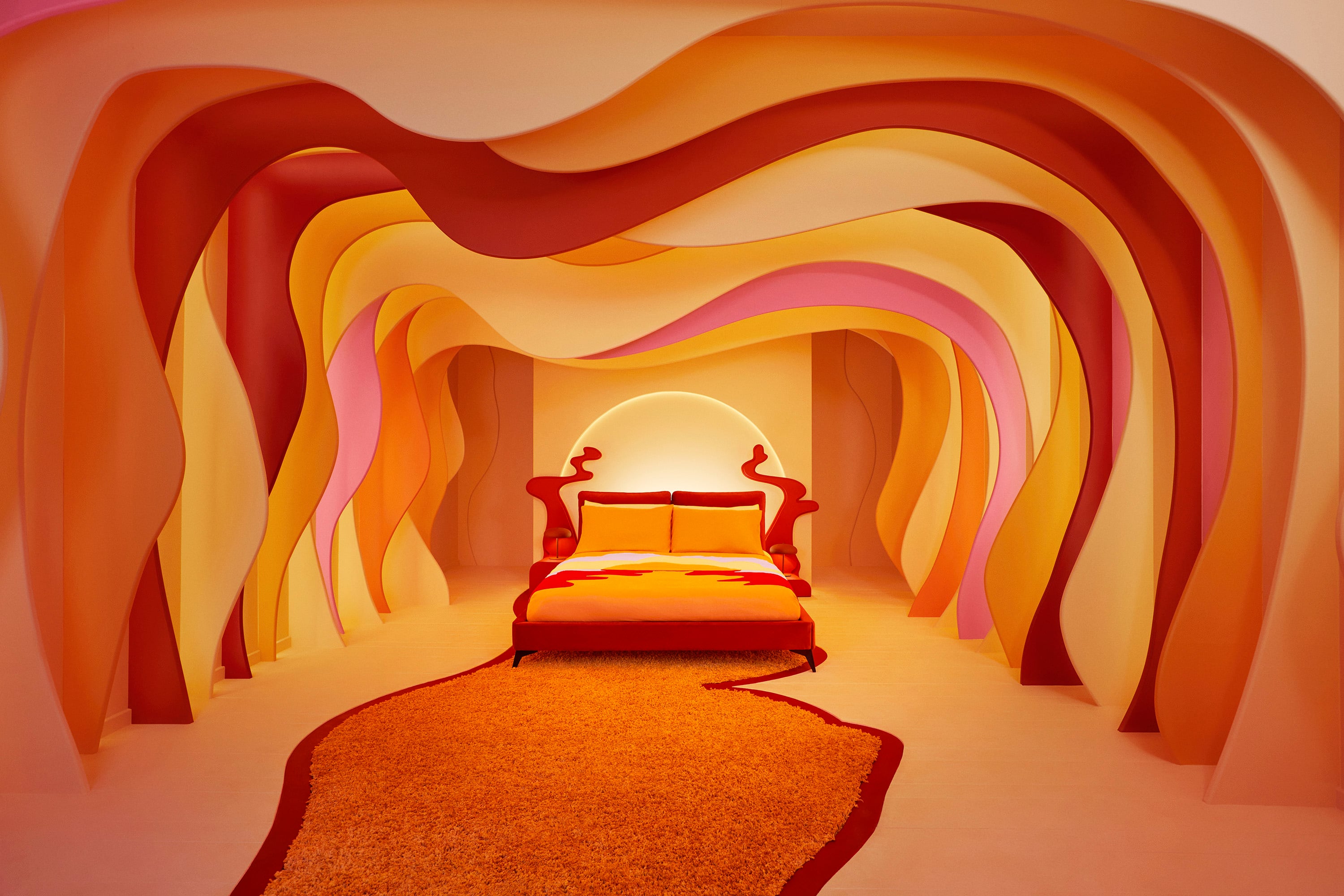 The sumptuous bed surrounded by red and orange waves that emulate the melting sunset colorways of the Sundown Cardigan. — Photo by Airbnb