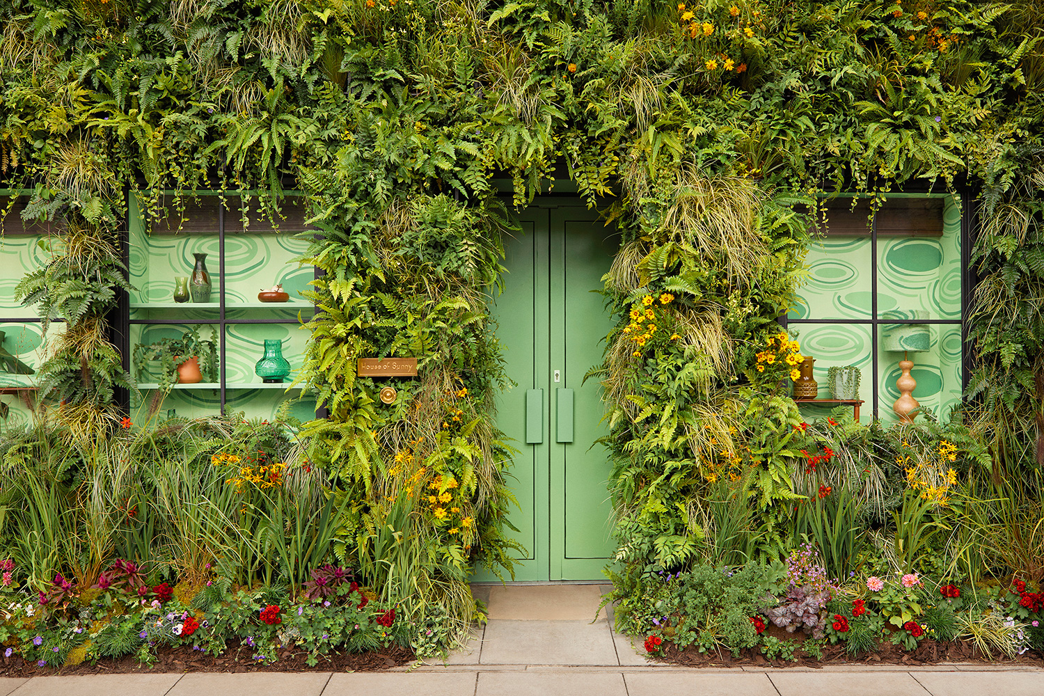 The green oasis entrance with real plants and flowers, inspired by the swirling green tones of Sunny’s famous Hockney Dress, as worn by celebrities. — Photo by Airbnb