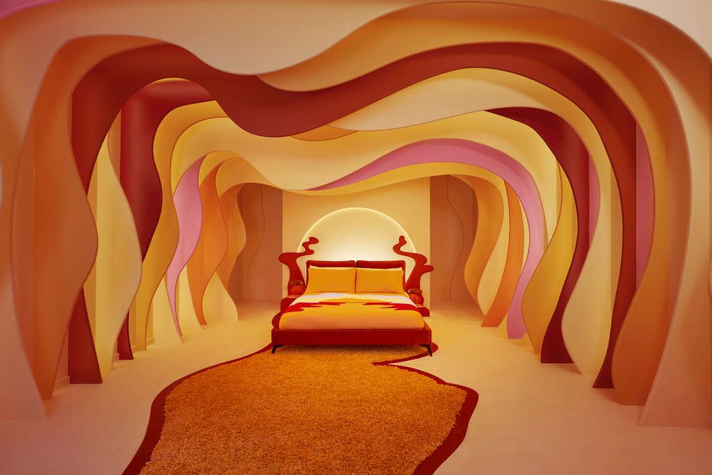 The sumptuous bed surrounded by red and orange waves that emulate the melting sunset colorways of the Sundown Cardigan. — Photo by Airbnb